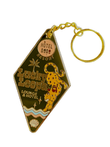 The Lucky Leopard Lounge Motel Keyring Olive by Hôtel Dodo features "Lucky Leopard Lounge & Hotel" with a leopard, palm trees, and a shell on gold enamel, attached to a round ring—ideal as a chic keychain or bag charm.