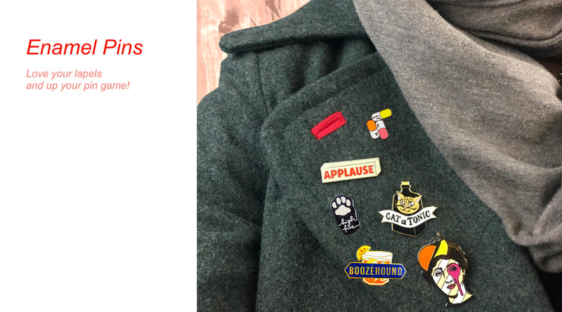 Gray coat with various enamel pins: red bar, "Applause," paw print, cat with "Cat Tonic," "Boozehound," and a colorful face. Text on left reads, "Enamel Pins: Love your lapels and up your pin game!.