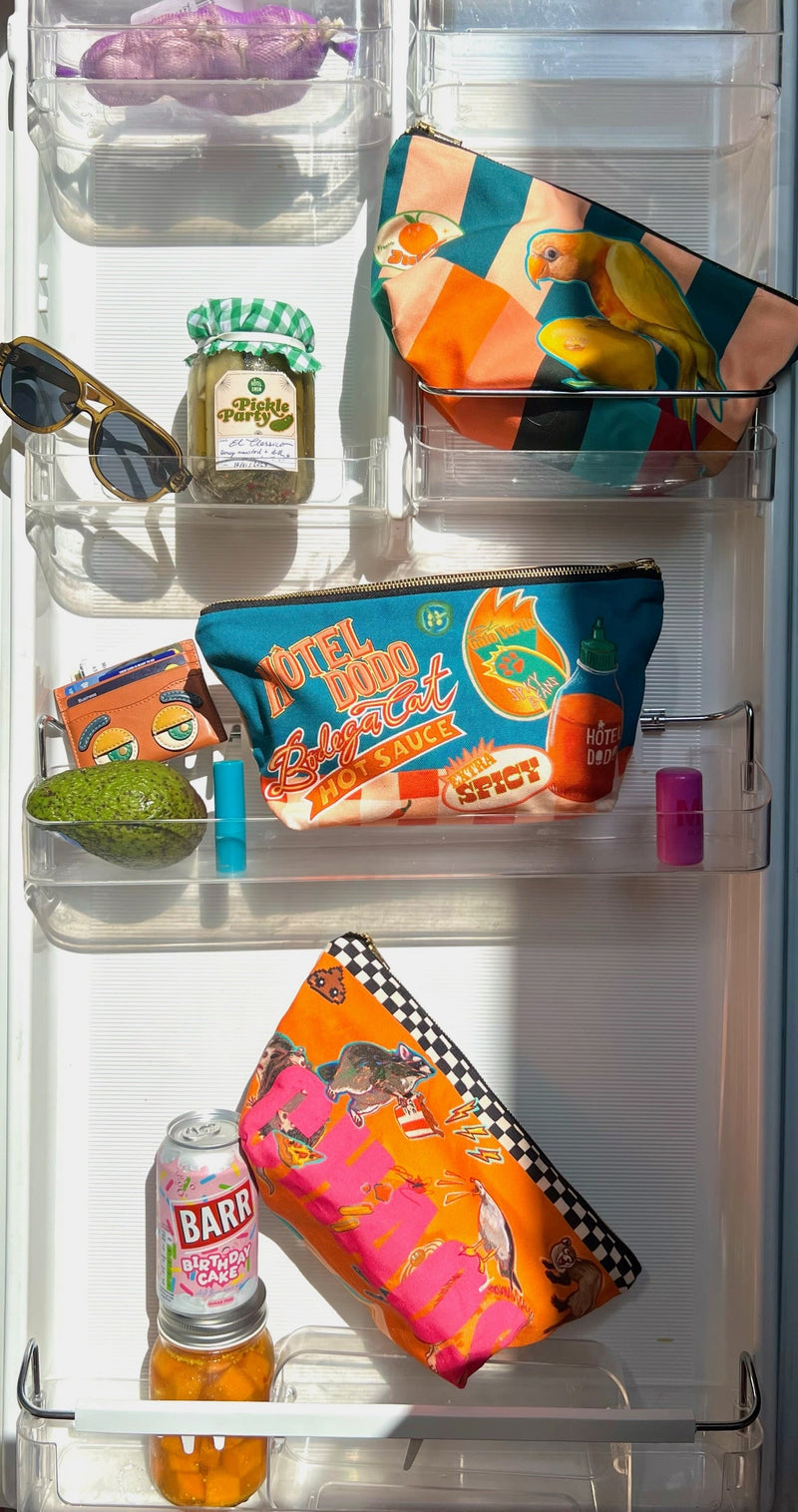 Various colorful pouches, a pair of sunglasses, jar of pickles, canned drink, lip balms, and avocado are arranged on clear refrigerator door shelves.