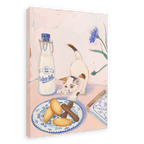 A kitten reaches for pastries on a plate beside a bottle of milk and a box labeled "Katzenzungen," the German word for "cats tongues." The scene is beautifully captured in the Hôtel Dodo Katzenzungen Giclée Canvas Print, featuring a blue flower and other small decorative items in the background.