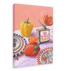 The "Hôtel Dodo Paprika Puszta Giclée Canvas Print" from Hôtel Dodo showcases a framed painting that depicts a yellow bell pepper, red pepper, a paprika box labeled "Hungarian paprika," and a red tulip on a table set with decorative plates and a pink-checkered cloth.