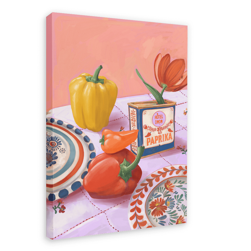 The "Hôtel Dodo Paprika Puszta Giclée Canvas Print" from Hôtel Dodo showcases a framed painting that depicts a yellow bell pepper, red pepper, a paprika box labeled "Hungarian paprika," and a red tulip on a table set with decorative plates and a pink-checkered cloth.