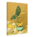 The Ikebana Banana Giclée Canvas Print by Hôtel Dodo showcases tropical foliage, yellow flowers, bananas in a bowl, a figurine, and a key tag labeled "Hôtel Dodo," all arranged on a striped surface set against a mustard-yellow background.