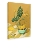 The Ikebana Banana Giclée Canvas Print by Hôtel Dodo showcases tropical foliage, yellow flowers, bananas in a bowl, a figurine, and a key tag labeled "Hôtel Dodo," all arranged on a striped surface set against a mustard-yellow background.