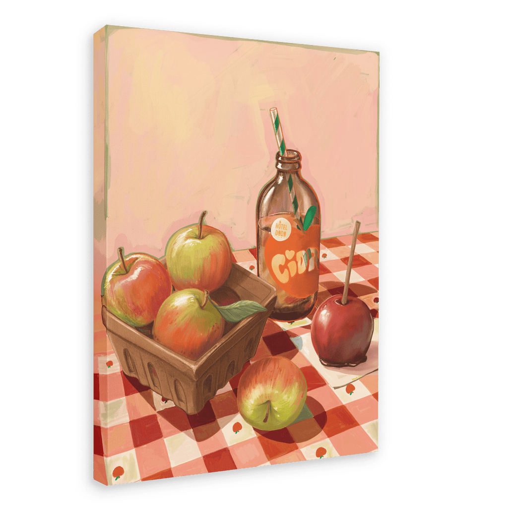 Hôtel Dodo’s “Apple Core Giclée Canvas Print” features a charming scene of apples in a carton, a glass bottle of fresh cider with a straw, a toffee candy apple, and a loose apple, all arranged on a red-checkered tablecloth set against a light pink background.
