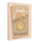 Tarot Cats’ “The Hanged Man Canvas Print” features a tarot card illustration of a cat hanging upside down by its tail from a branch, with sun rays in the background.