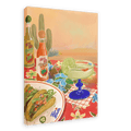 Sure! Here’s a revised version using the product data: A vibrant painting titled “Taco Belle Giclée Canvas Print” by Hôtel Dodo features crunchy tacos on a plate, a zesty margarita garnished with lime, two bottles of Bodega Cat Hot Sauce, and cactus plants set against a desert backdrop atop a red floral tablecloth.