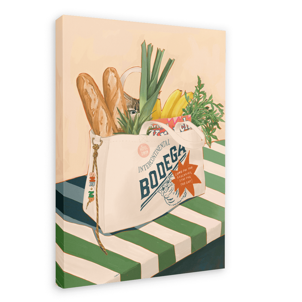 The Bodega Bounty Giclée Canvas Print by Hôtel Dodo features a grocery bag brimming with baguettes, leeks, bananas, carrots, and packaged food atop a green-and-white striped table—a delightful scene reminiscent of the kind a vigilant Bodega cat might guard.