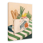 The Bodega Bounty Giclée Canvas Print by Hôtel Dodo features a grocery bag brimming with baguettes, leeks, bananas, carrots, and packaged food atop a green-and-white striped table—a delightful scene reminiscent of the kind a vigilant Bodega cat might guard.