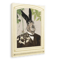 The Hare In A Suit Canvas Print by Animals In Suits features a portrait of Mister Hare, a rabbit with black-tipped ears dressed in a dark suit, posed before cascading flowers and lush greenery crafted from vintage botanical illustrations, all elegantly framed with an ornate cream border.