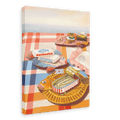 The “Dishy Fishy Giclée Canvas Print” by Hôtel Dodo depicts a picnic table adorned with retro fish plates filled with tinned fish, anchovies, and other treats on a red and white checked tablecloth by the water—perfectly capturing the charm of summer girl dinners.