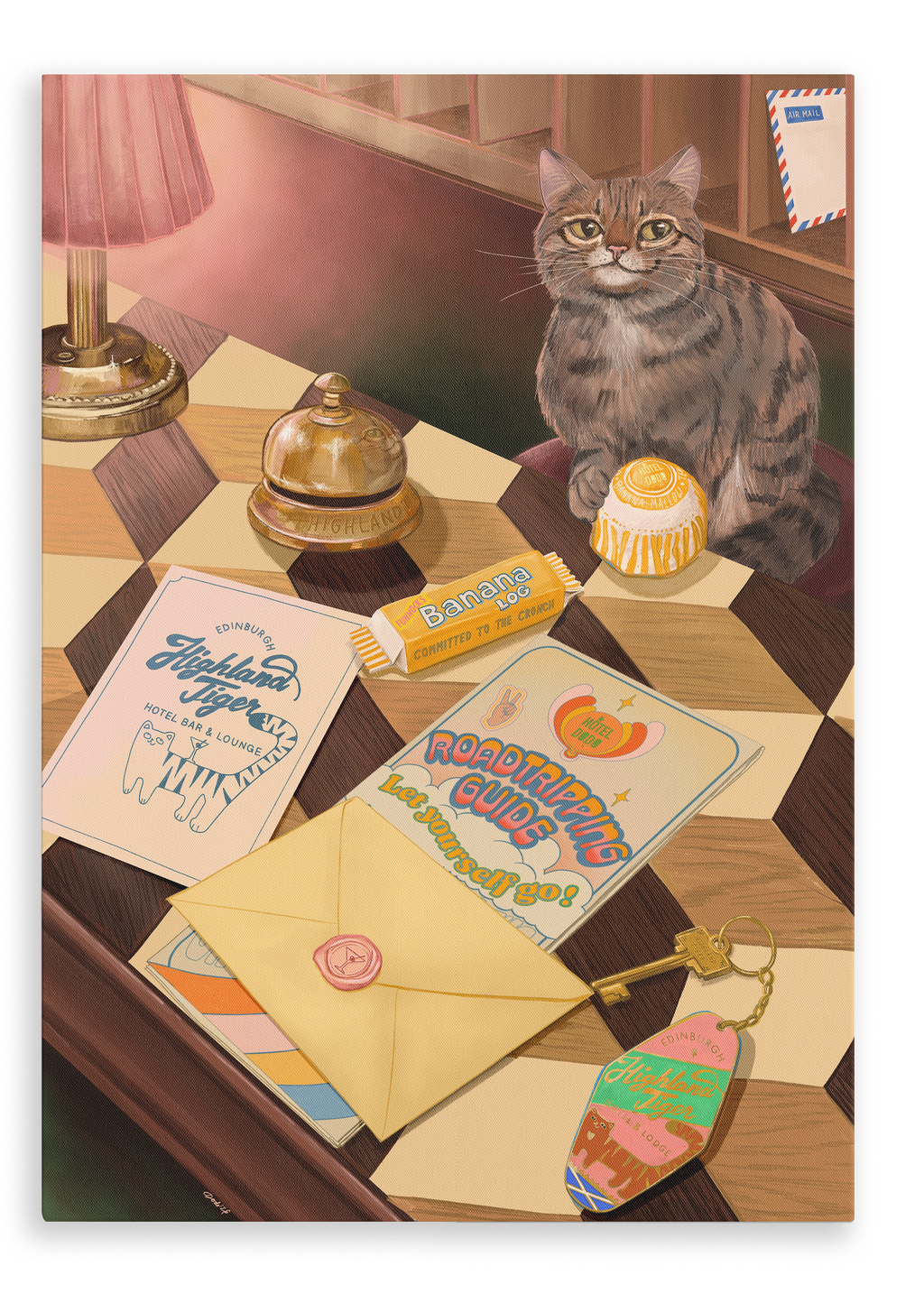 A tabby cat sits on a checkered table beside travel items—including postcards, an envelope, a banana candy, a bell, a keychain, and a round yellow candy—while the Highland Tiger Lodge Giclée Canvas Print by Hôtel Dodo is displayed nearby.