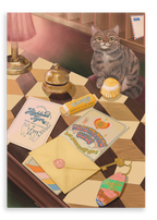 A tabby cat sits on a checkered table beside travel items—including postcards, an envelope, a banana candy, a bell, a keychain, and a round yellow candy—while the Highland Tiger Lodge Giclée Canvas Print by Hôtel Dodo is displayed nearby.