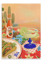 A zesty margarita with a lime slice, crunchy tacos on a plate, and bottles of Bodega Cat Hot Sauce are beautifully arranged on a floral tablecloth adorned with cacti and a vibrant desert landscape in the background, as depicted in the “Taco Belle Giclée Canvas Print” by Hôtel Dodo.