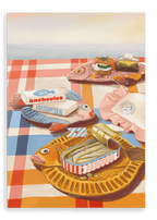 Three Dishy Fishy Giclée Canvas Prints by Hôtel Dodo, featuring food and retro dinnerware details, are arranged atop a red and white checkered tablecloth alongside tinned fish containers and a folded pink napkin with text.