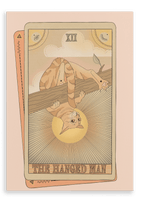 The Hanged Man Canvas Print by Tarot Cats depicts an orange cat hanging upside down from a branch as the central focus, with two partially visible tarot cards in the background.