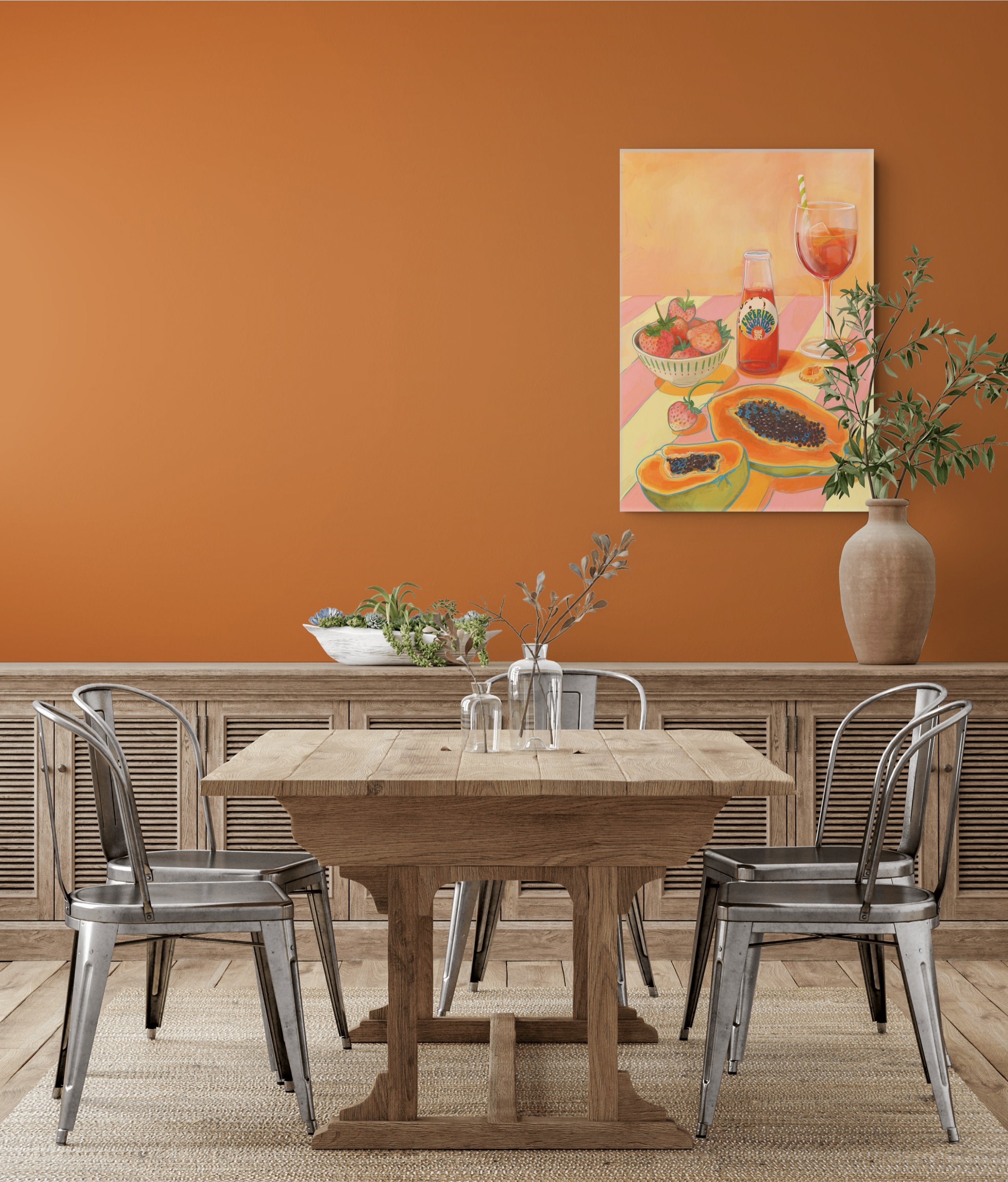 A wooden dining table with four metal chairs sits in front of an orange wall, adorned with Hôtel Dodo’s L’Aperitivo Leopardo Giclée Canvas Print and a large vase with branches—evoking the relaxed charm of an Indian summer picnic at Hôtel Dodo.
