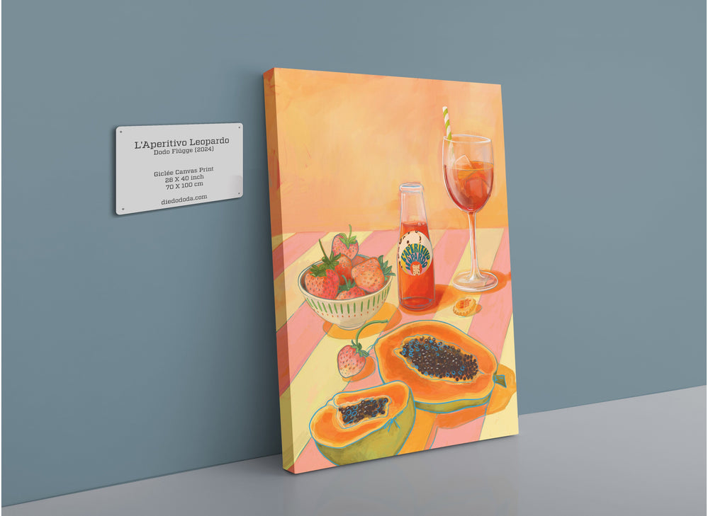 The L'Aperitivo Leopardo Giclée Canvas Print by Hôtel Dodo showcases a table setting adorned with a vermouth drink, strawberries, and halved papayas set against an orange and pink background that evokes the feeling of an Indian summer picnic. A label detailing the artwork is affixed to the wall.