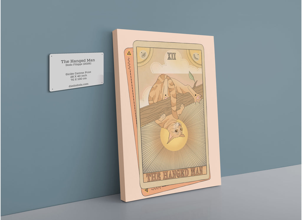 A framed illustration of The Hanged Man Canvas Print by Tarot Cats leans against a blue wall next to a plaque displaying the product’s name, brand, print size, and website.