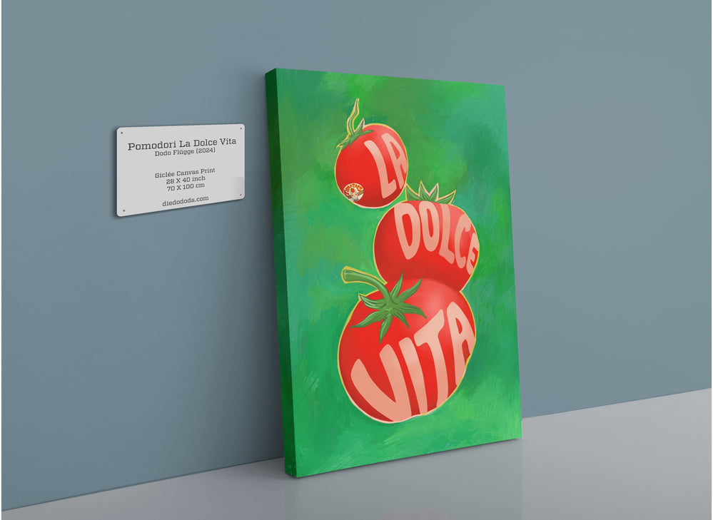 The Pomodori La Dolce Vita Giclée Canvas Print by Intercontinental Fruitery features three red tomatoes, each inscribed with a word from the phrase "La Dolce Vita," displayed on a green background. A small plaque with the artwork details is mounted next to it.