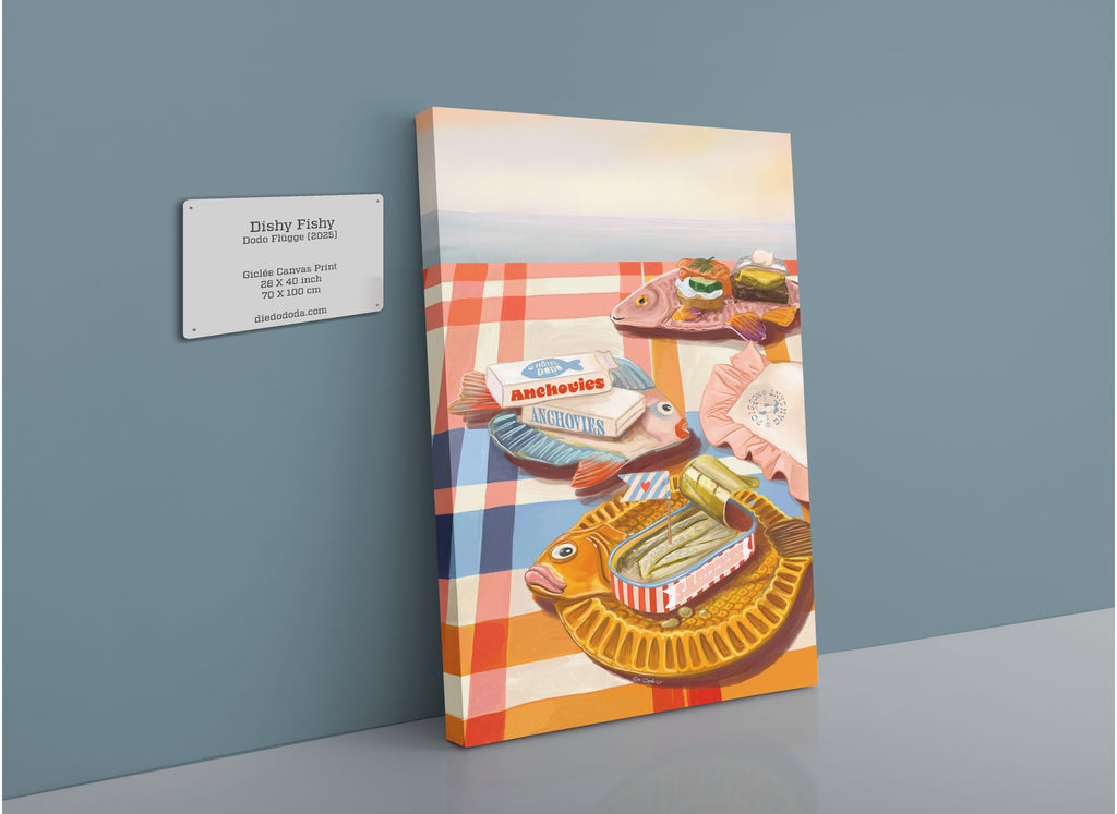 A vibrant giclée canvas print from Hôtel Dodo titled “Dishy Fishy” features colorful retro fish plates, each uniquely shaped and brimming with food—a playful reference to the tinned fish trend—arranged atop a checkered tablecloth and displayed alongside a sign listing artwork details.
