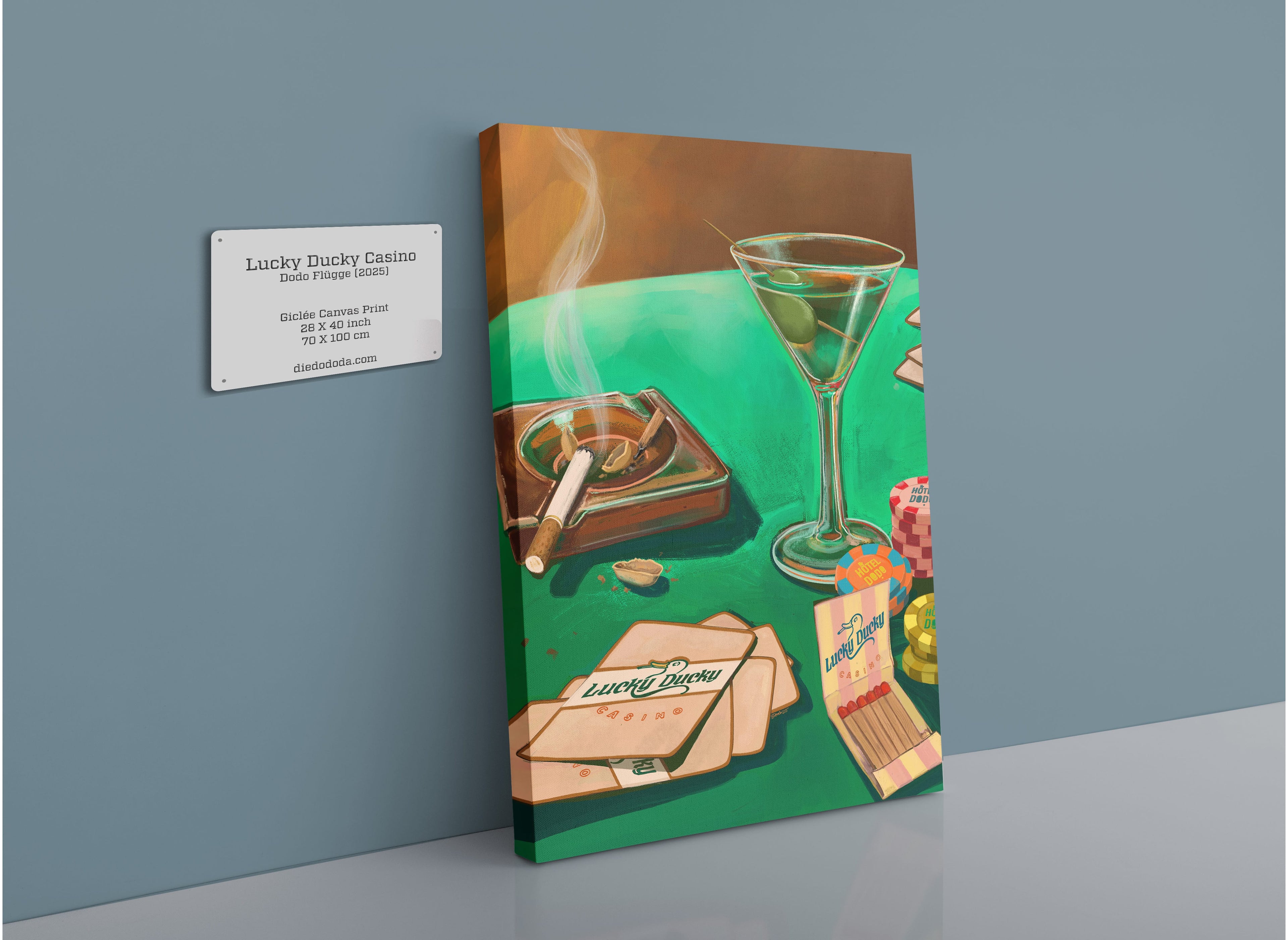 The Lucky Ducky Casino Giclée Canvas Print by Hôtel Dodo features a vivid scene of a cocktail, smoking cigar, poker chips, playing cards, matchbook, and ashtray atop a green table—capturing the dynamic atmosphere of the casino—beautifully displayed on a light blue wall with an accompanying small sign.