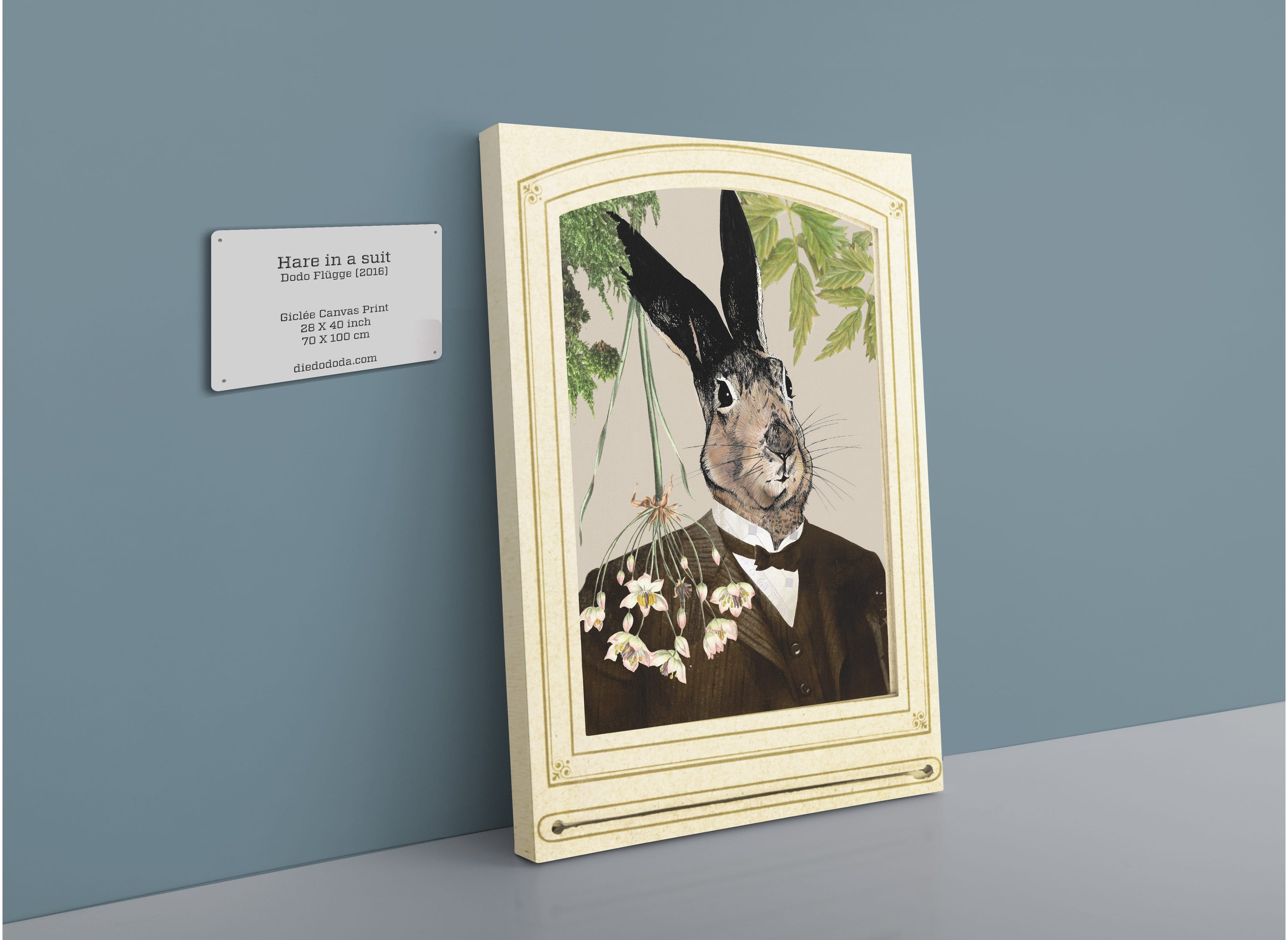 The Hare In A Suit Canvas Print by Animals In Suits features a whimsical, handmade collage of Mister Hare dressed in a suit, displayed on a shelf against a blue wall. A nearby wall label reads “Hare in a suit,” enhancing the vintage botanical illustration feel of this charming framed artwork.