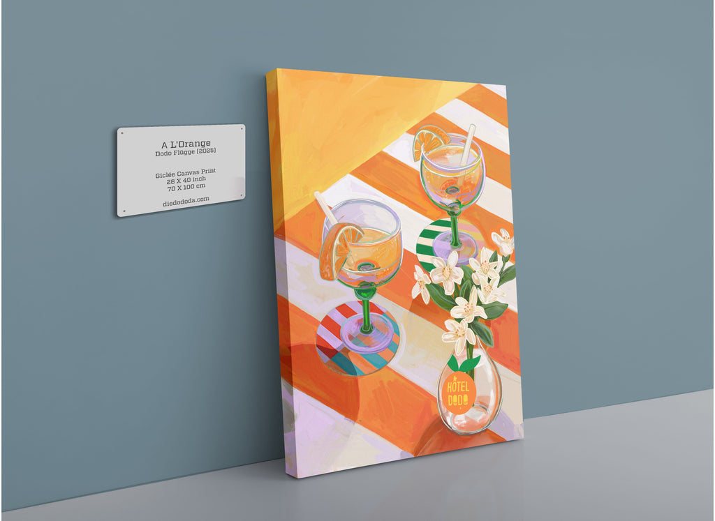 Bring vibrant style to your space with the “A L’Orange” Giclée Canvas Print by Hôtel Dodo, featuring cocktails, orange slices, and white neroli blossoms on a striped table—an ideal choice for fans of curated table settings.