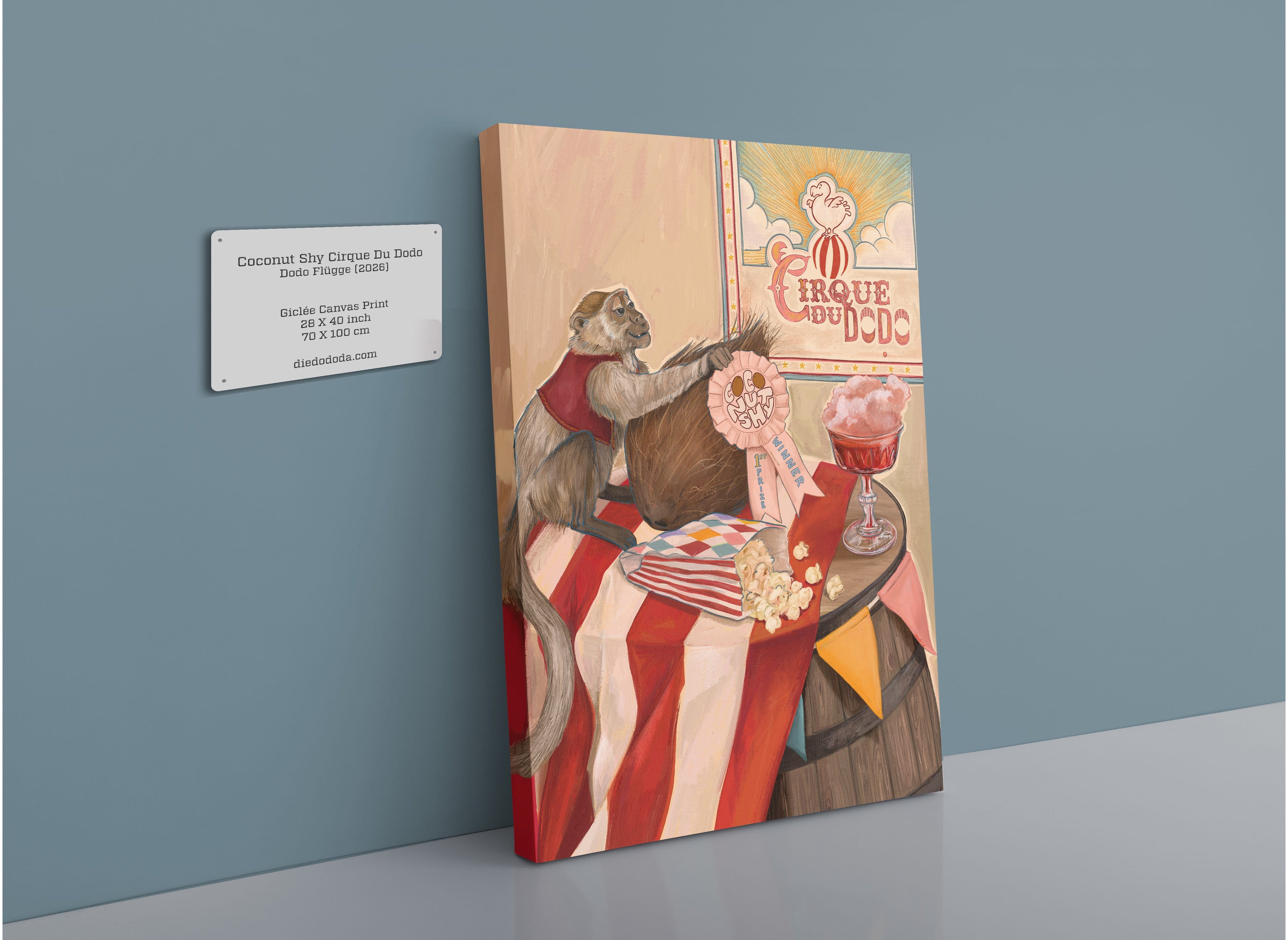 A giclée canvas print by Hôtel Dodo, titled “Coconut Shy Cirque Du Dodo,” depicts a monkey dressed in circus attire alongside a coconut, popcorn, and a pink drink—suggestive of an imaginative cotton candy cocktail—set near a Cirque du Dodo sign. A wall label provides artwork details, capturing the playful essence of vintage circus games.