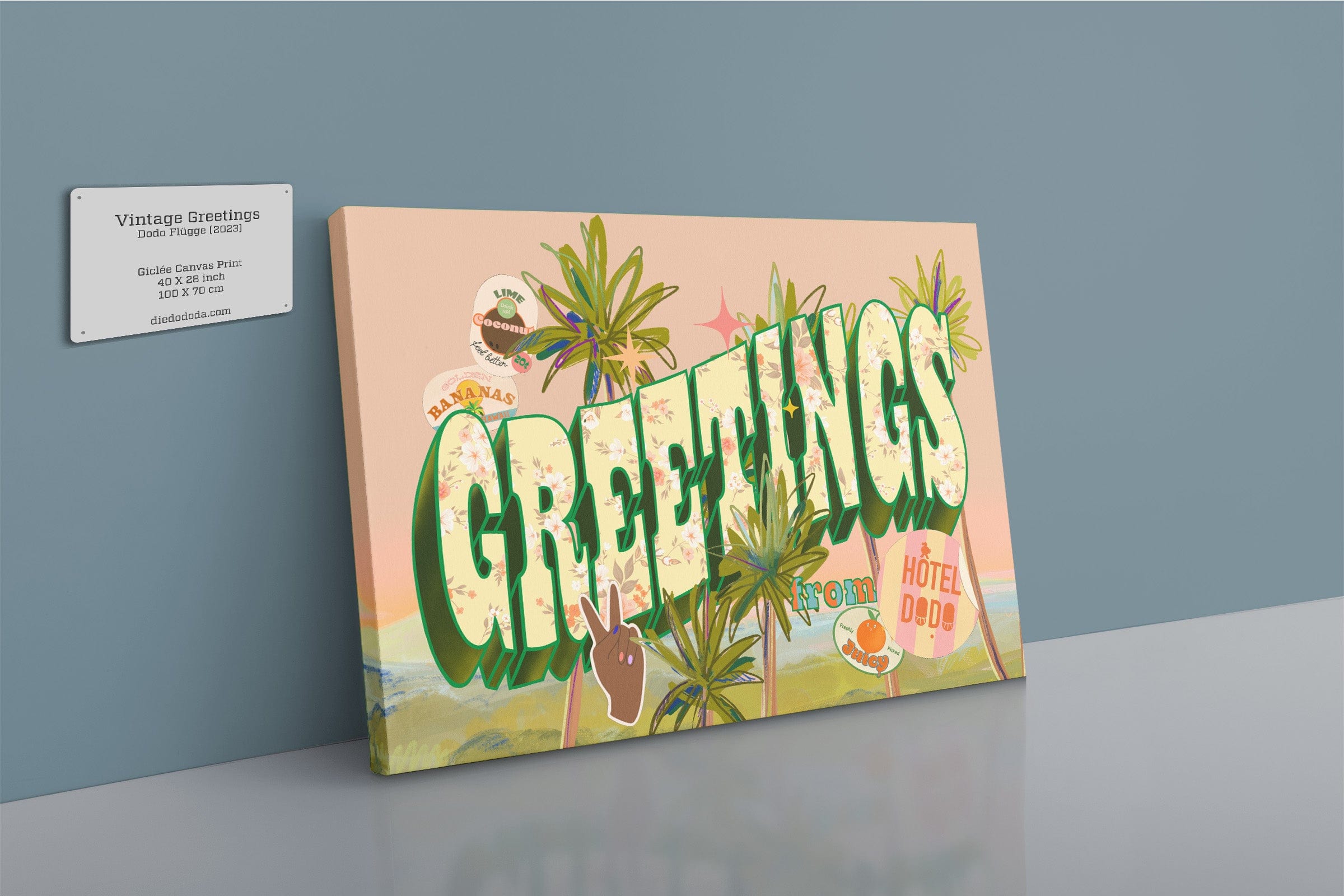 The Shromps Vintage Greetings Matte Canvas Print, featuring large “GREETINGS” text with palm trees and postcard-style stickers, is displayed on a shelf beside a business card against a light blue wall.