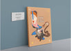 Spicy Boots Giclée Canvas Print titled "spicy showdown" hanging on a blue wall, featuring a playful illustration of a cat wearing boots, surrounded by whimsical elements. A description plaque is mounted next to it. Created by Kitsch Kanaveral.