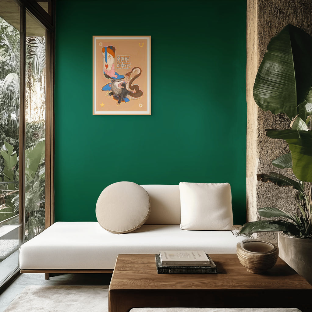 Minimalist living room with a white sofa, round cushion, wooden table, green accent wall, and large plant beneath a glass door overlooking greenery—subtle accents like the Spicy Boots Giclée Art Print by Kitsch Kanaveral and a decorative ceramic snake on the table add personality and charm.