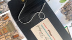 A black envelope with string closure rests on illustrated Edinburgh art prints, labeled “Edinburgh Mini Print Set | 15 A6 Original Drawings” by Essential Edinburgh—an ideal Scotland gift or unique souvenir.
