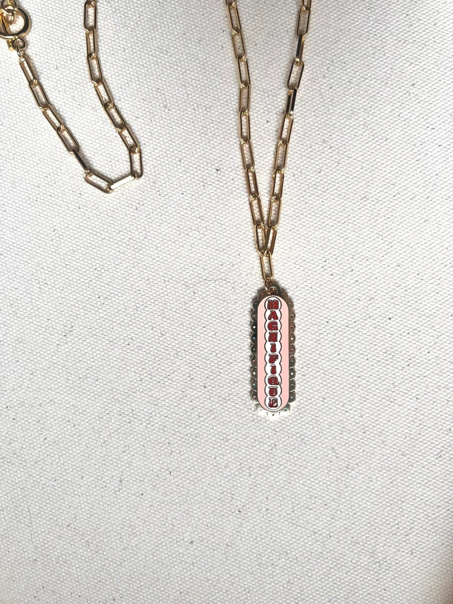 Magnifique Necklace with a medium paperclip chain and a scalloped pendant featuring a red and white design on a textured fabric surface by Necklaces.
