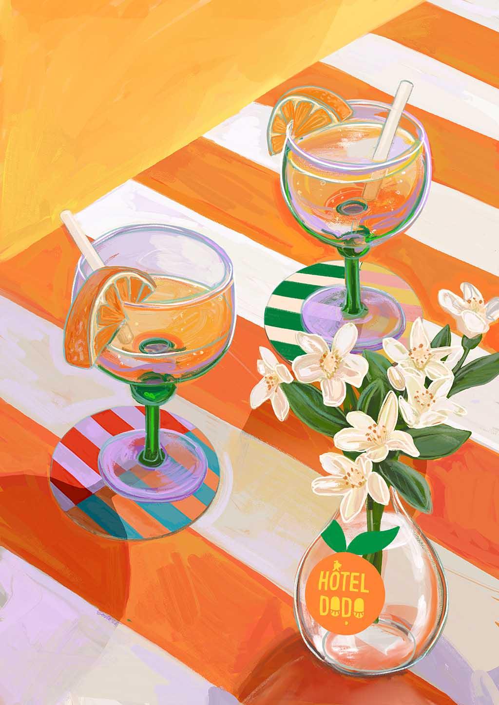 Two margarita glasses with orange slices and straws rest on a striped table beside a vase of white flowers, styled next to the Hôtel Dodo 