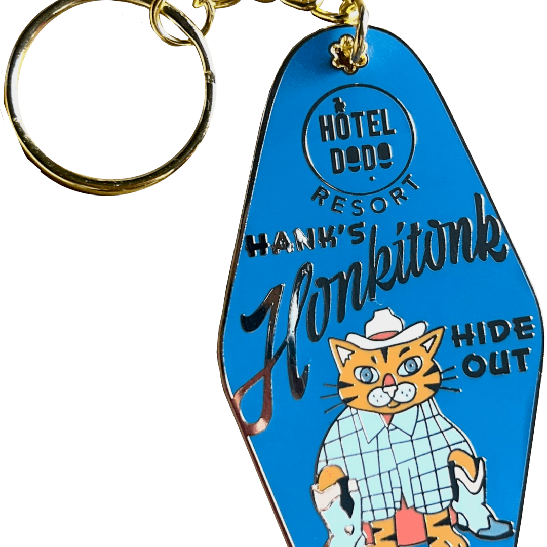 The Hank's Honkitonk Hideout Keyring Blue by Hôtel Dodo features a cat cowboy and rustic accents, with 