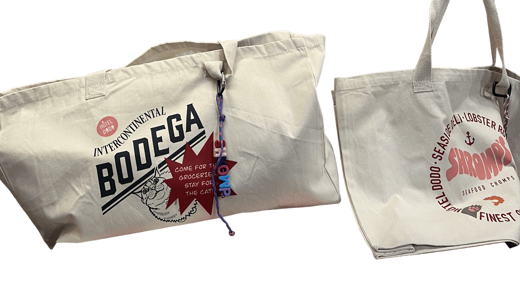 The Bodega/Shromp’s XXL Snack Shopper by Bags by diedododa includes two UK-made, eco-friendly cotton totes: one with a Bodega and cat design, the other seafood-themed with "Shrimp." Both are stylish and sustainable choices.