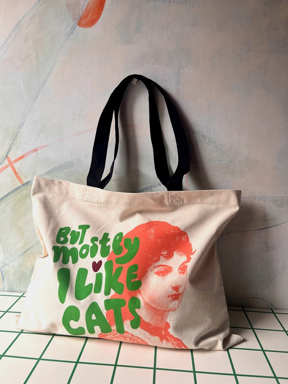 The "But Mostly I Like Cats Shopping & Beach Bag" by Bags by diedododa is a cotton canvas tote featuring black handles and a vintage-style portrait of a woman, accompanied by the text "BUT MOSTLY I LIKE CATS" in vibrant green and red lettering. It's ideal for cat lovers to carry their favorite snacks or essentials.