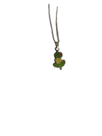 The Canapé Cutie Necklace by Necklaces features a silver chain with a pendant shaped like a green cartoon alien in a flying saucer.