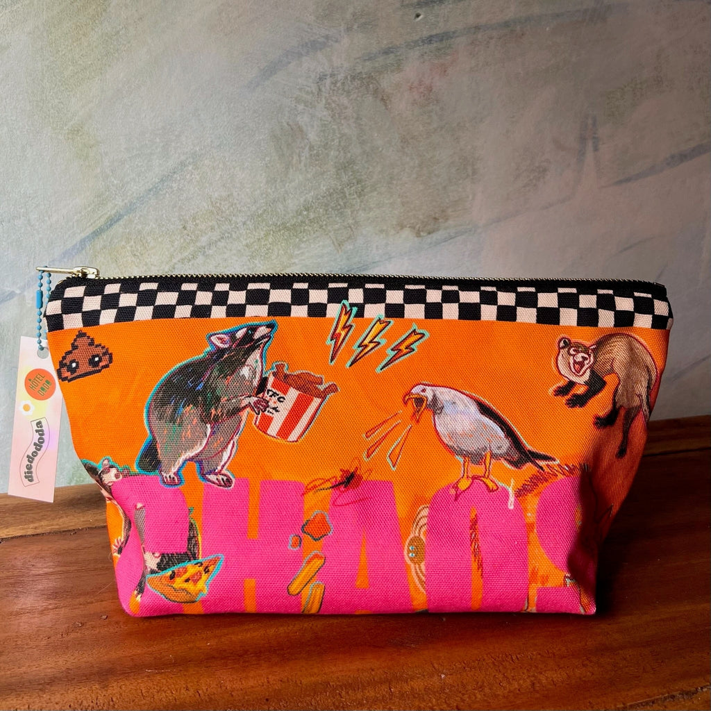 The Chaos Creatures Pouch by Aventures Des Créatures is an orange zipper pouch with possum, bird, and weasel art, a checkered band, side tag, and is handmade in the UK.