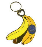 The Chonkita Banana Keyring by Hôtel Dodo features two yellow bananas—one with a blue "Chiquita" sticker—on a gold ring, making a quirky and fun bag charm.