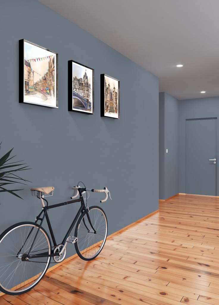 A black bicycle stands against a blue wall in a hallway with wooden floors and recessed lighting, featuring three Essential Edinburgh "North Bridge & The Balmoral Edinburgh" matte art prints.