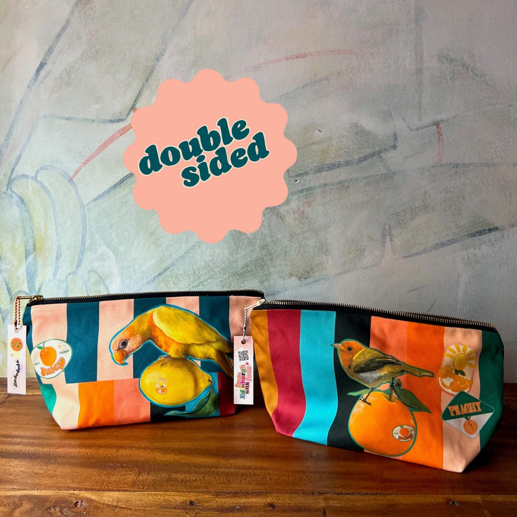 Sticky Beaks Pouch by Sticky Beaks: Two vibrant zip pouches featuring bird and fruit designs, displayed on wood under a "double sided" sign. Ideal as a handmade gift, these UK market day pouches bring charm to your essentials.