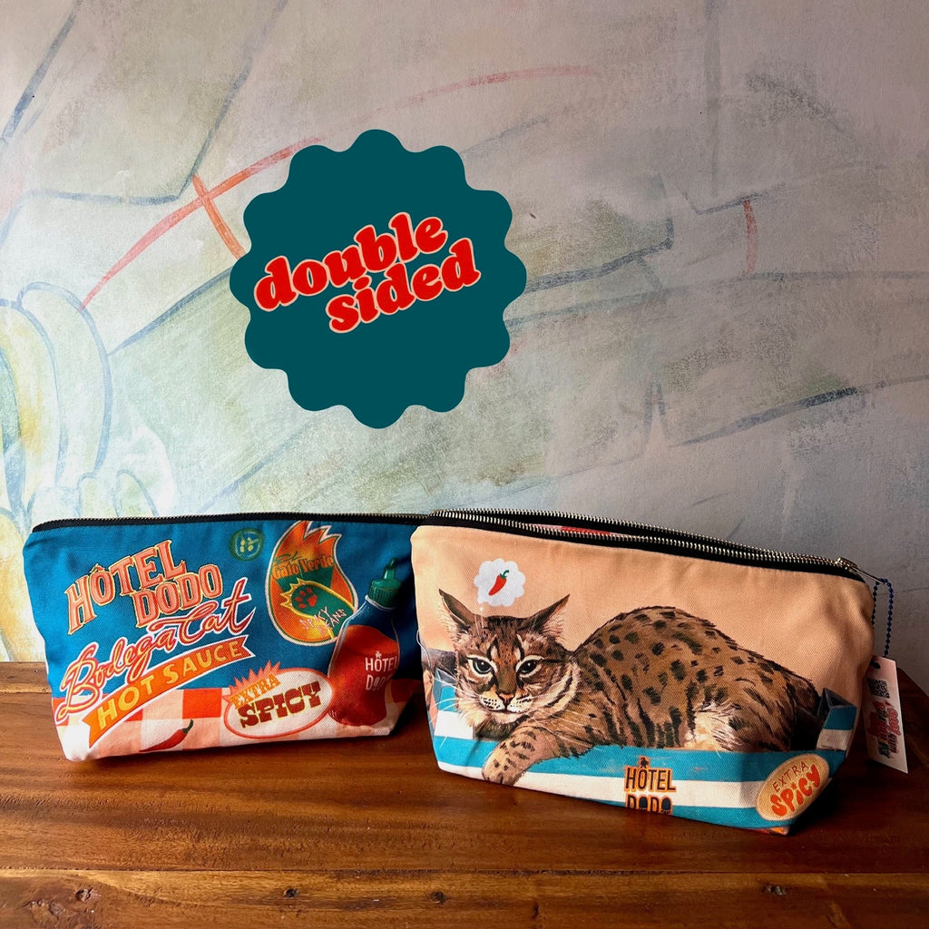 The Hôtel Dodo Bodega Cat Hot Sauce Pouch, a handmade UK item, features a hot sauce design on one side and an illustrated wildcat on the other, with a "double sided" label above the zippered pouches.