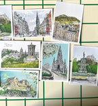 The Edinburgh Mini Print Set by Essential Edinburgh features 15 original A6 drawings of landmarks on a cream and green grid background—perfect as unique art prints or a memorable Scotland gift.