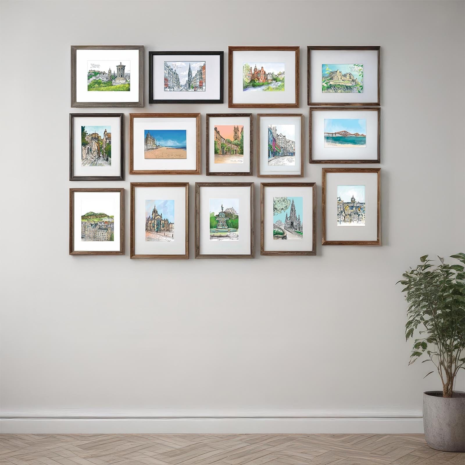 The Enchanting Edinburgh Mini Art Print Set by Essential Edinburgh features framed landscape and architectural paintings of city landmarks, arranged in a grid on a light wall above a potted plant.