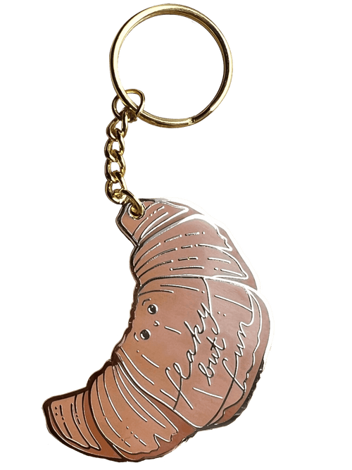 The Hôtel Dodo Kwasong Keyring features a croissant-shaped charm and an enamel tag engraved with "flaky but fun," making it a playful accessory for your keys or bag.