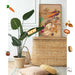 Room corner with a potted plant, wicker basket, and the colorful Earthly Delights Giclée Art Print by Kitsch Kanaveral, featuring charming vegetables and animals. Decorative elements include a ladybug, mushrooms, a carrot, leaves, and a banner reading "NEW Earthly Delights" in celebration of the harvest festival.