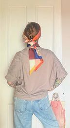 Person facing away from the camera, wearing a taupe shirt, light blue jeans, and the diedododa Hotel Dodo Scarf tied in their hair for a subtle color pop, standing in front of a white door.
