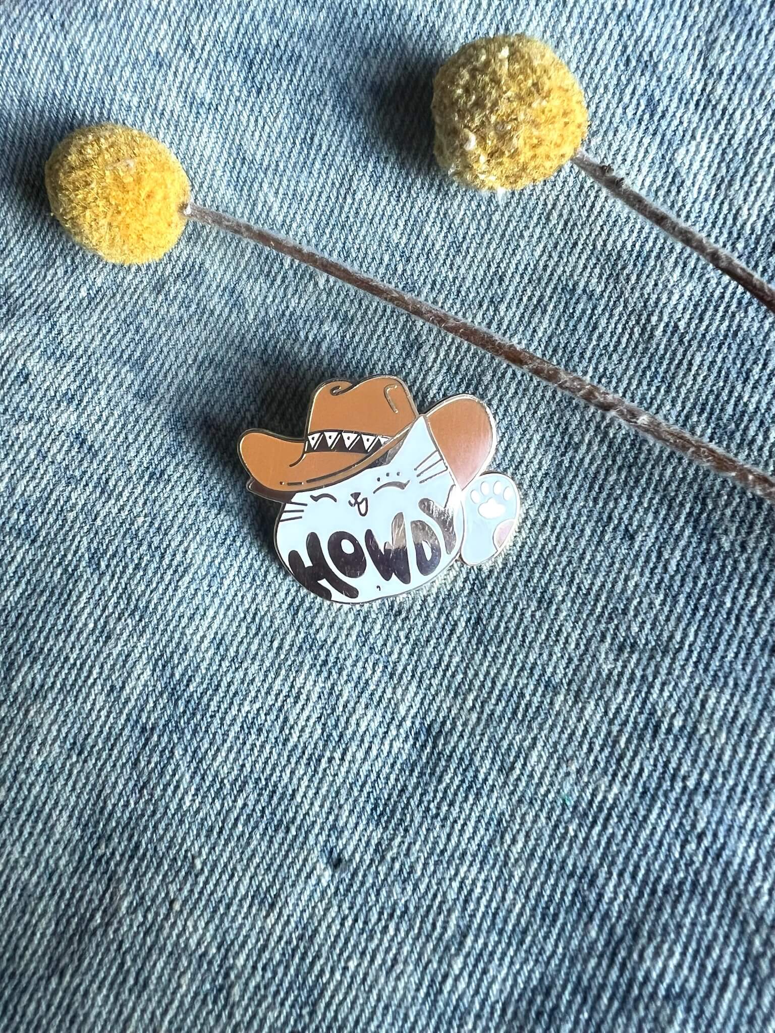 The Howdy Pawdner pin by Pins by diedododa features a cartoon cat, resembling a lucky cat, wearing a cowboy hat with 